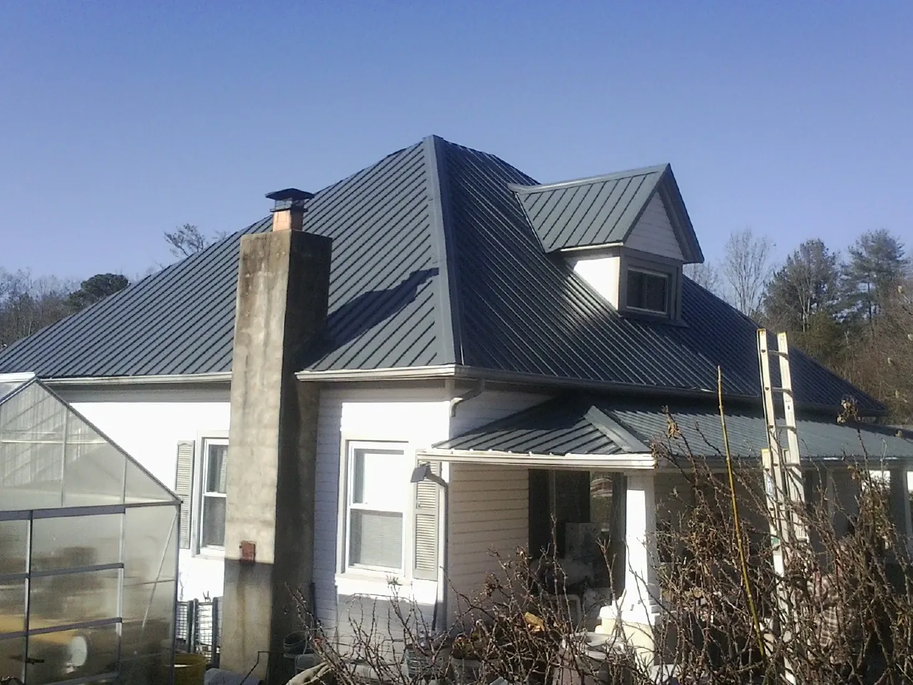 Dark blue standing seam metal roof on a white farmhouse with dormer — Slate & Tile Roof Repair by Roofing Brothers in Creedmoor