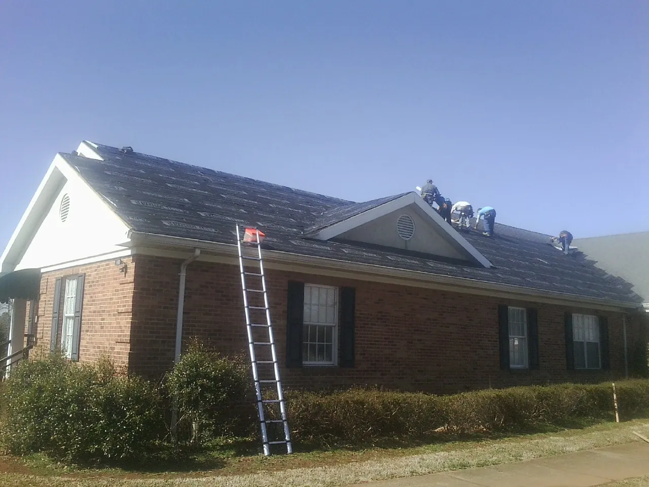 Crew tearing shingles off a brick ranch roof with a ladder set — Emergency Roof Repair work by our crew in Creedmoor