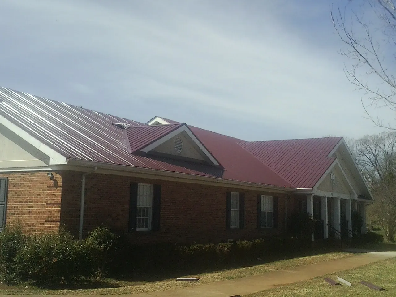 Red metal roof with gabled entries on a long brick building, from a Hail Damage Roof Repair job in Creedmoor