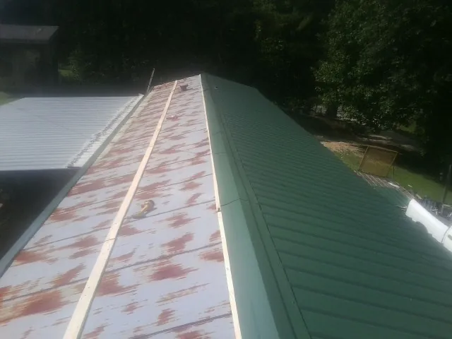Old rusted panels beside newly installed green metal roofing — Wind Damage Roof Repair by Roofing Brothers in Creedmoor