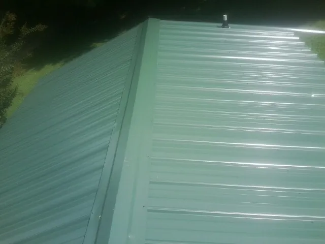New green metal panels meeting at the ridge of a roof — Flat Roof Repair work by our crew in Creedmoor