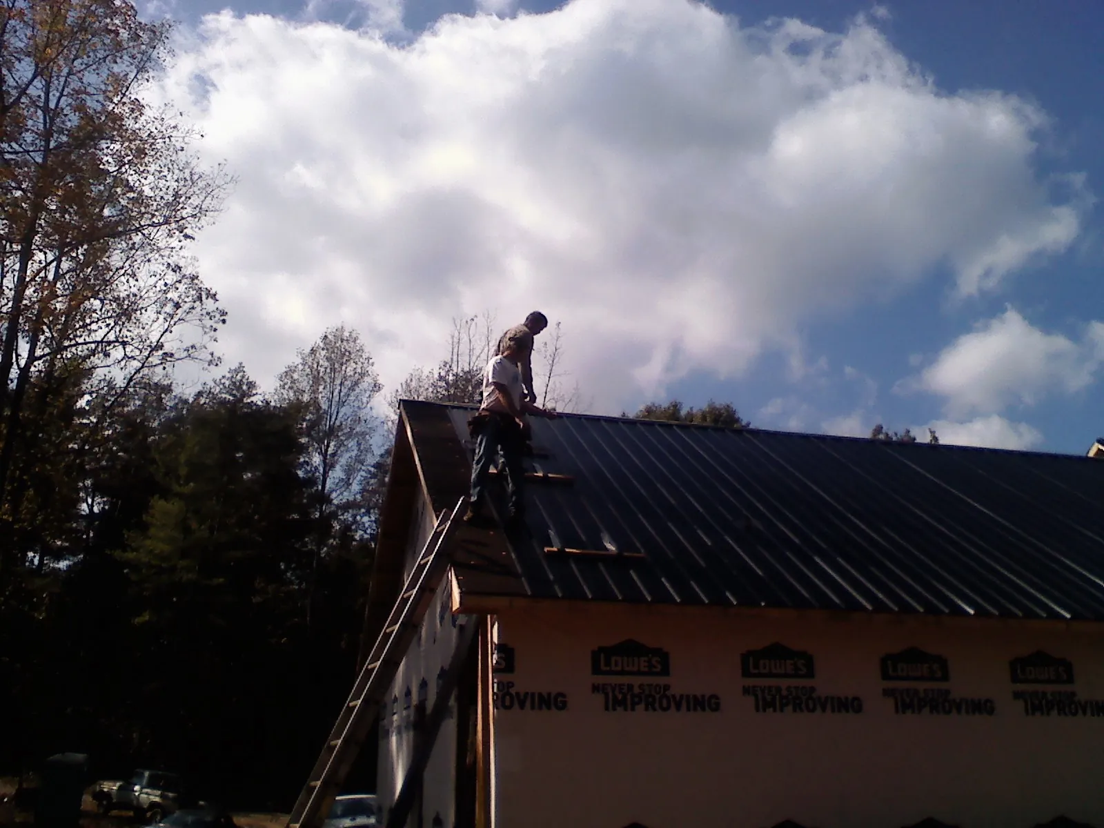 Roofer fastening dark metal panels high against a cloudy sky, from a Roof Inspection job in Creedmoor