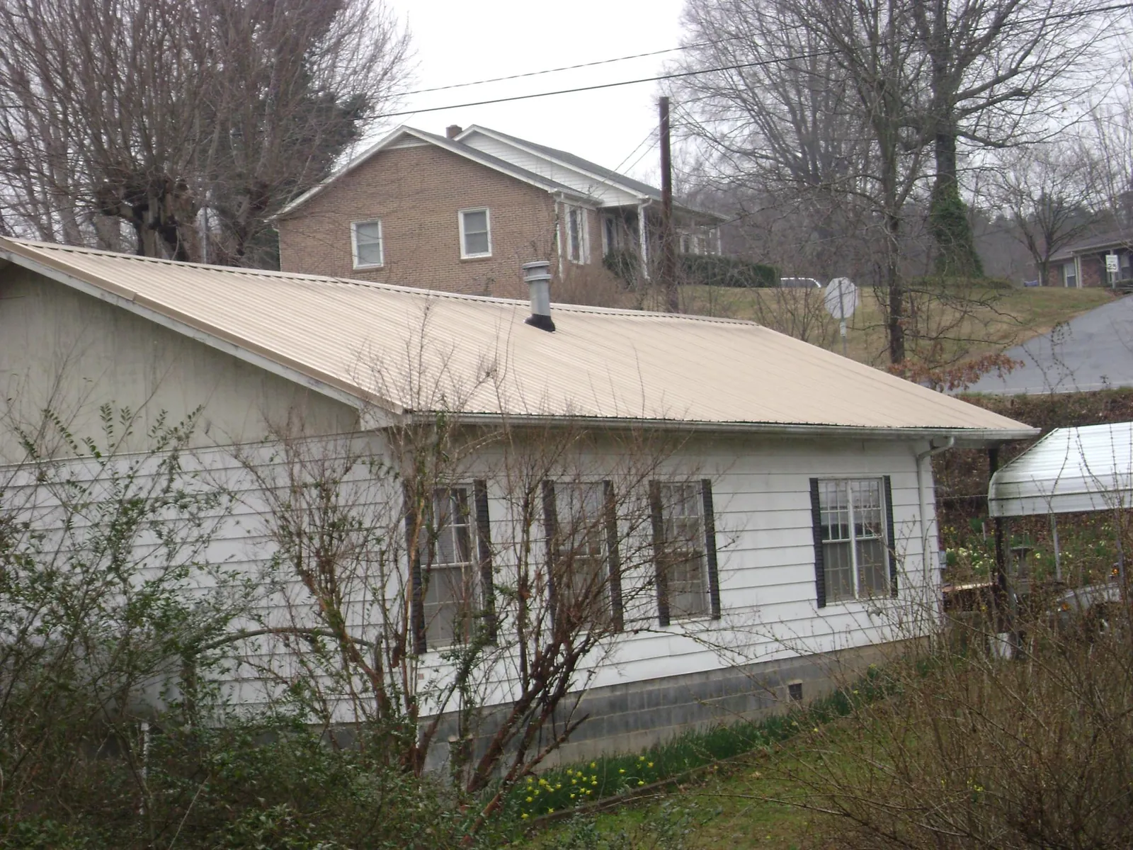 Tan metal roof on a white sided house set into a hillside — Commercial Roofing by Roofing Brothers in Creedmoor