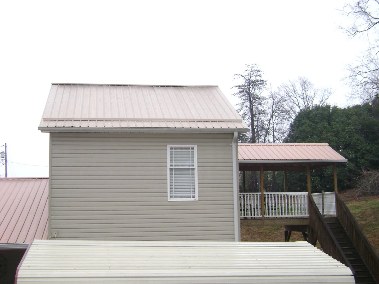 Tan metal roofs on a two story addition and attached porch, from a Roof Replacement job in Creedmoor