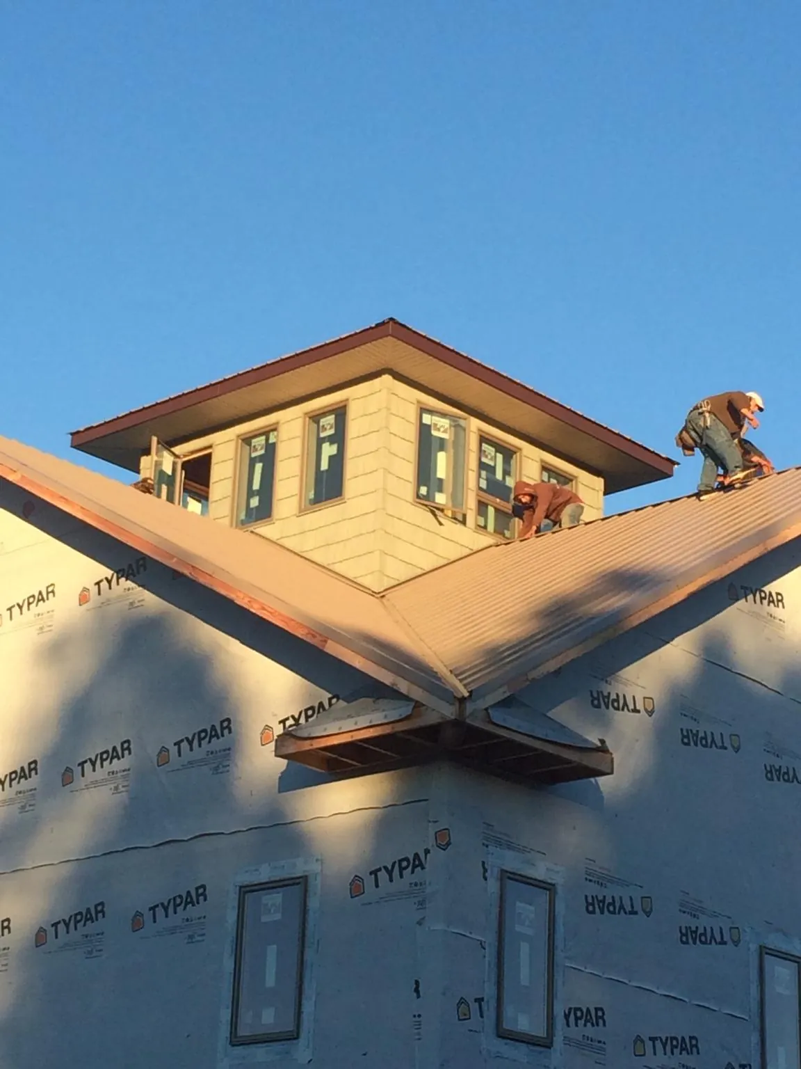 Roofers working around a rooftop cupola on a new metal roof at sunset — Roof Waterproofing in Creedmoor by Roofing Brothers